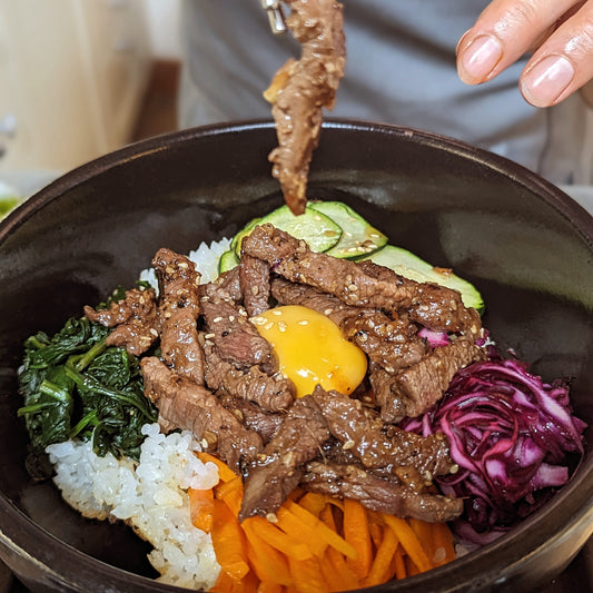 Beef bibimbap with namul and egg yolk, lifted with chopsticks